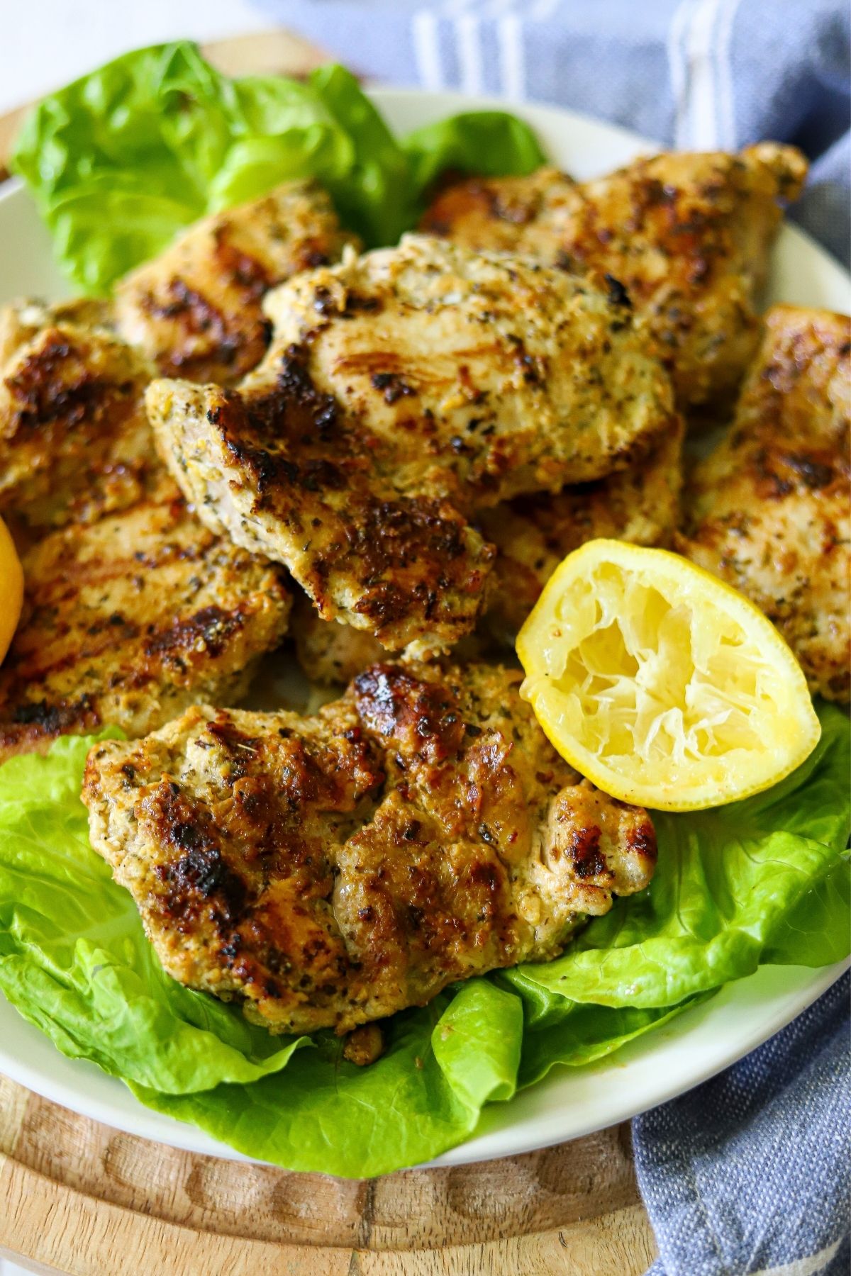 Grilled chicken thighs on a  bed of lettuce with squeezed lemon halves on the side. 