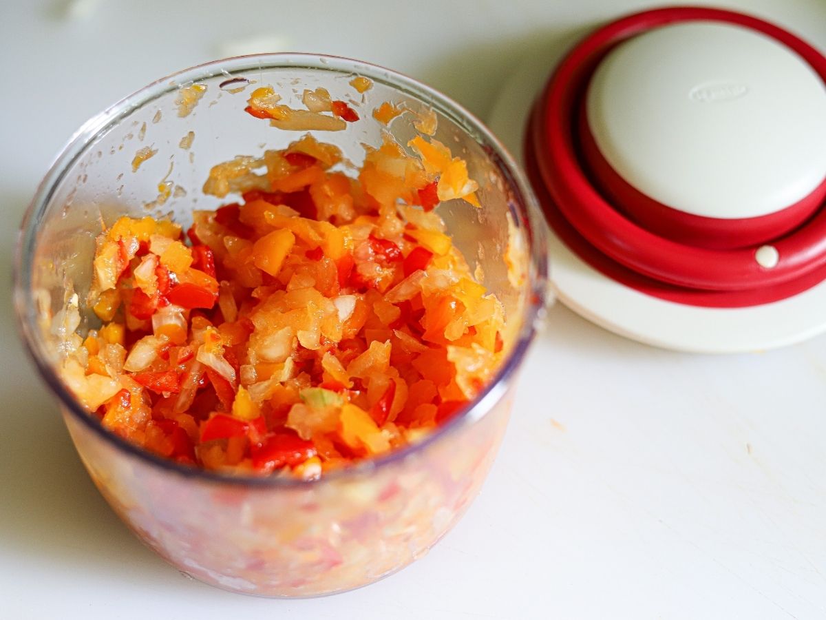 onions and bell peppers diced together in the bowl of a small food chopper. 