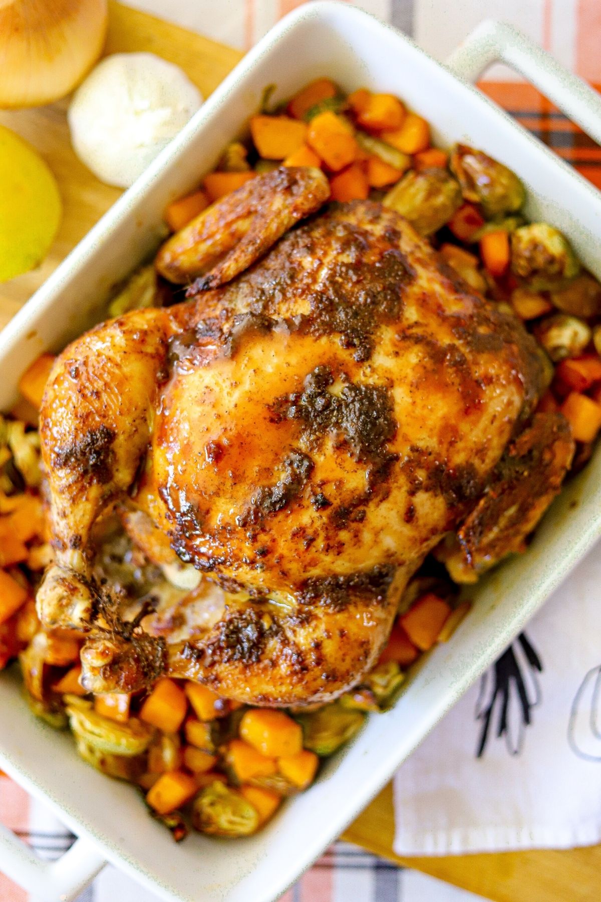 A whole roasted chicken over vegetables in a baking dish