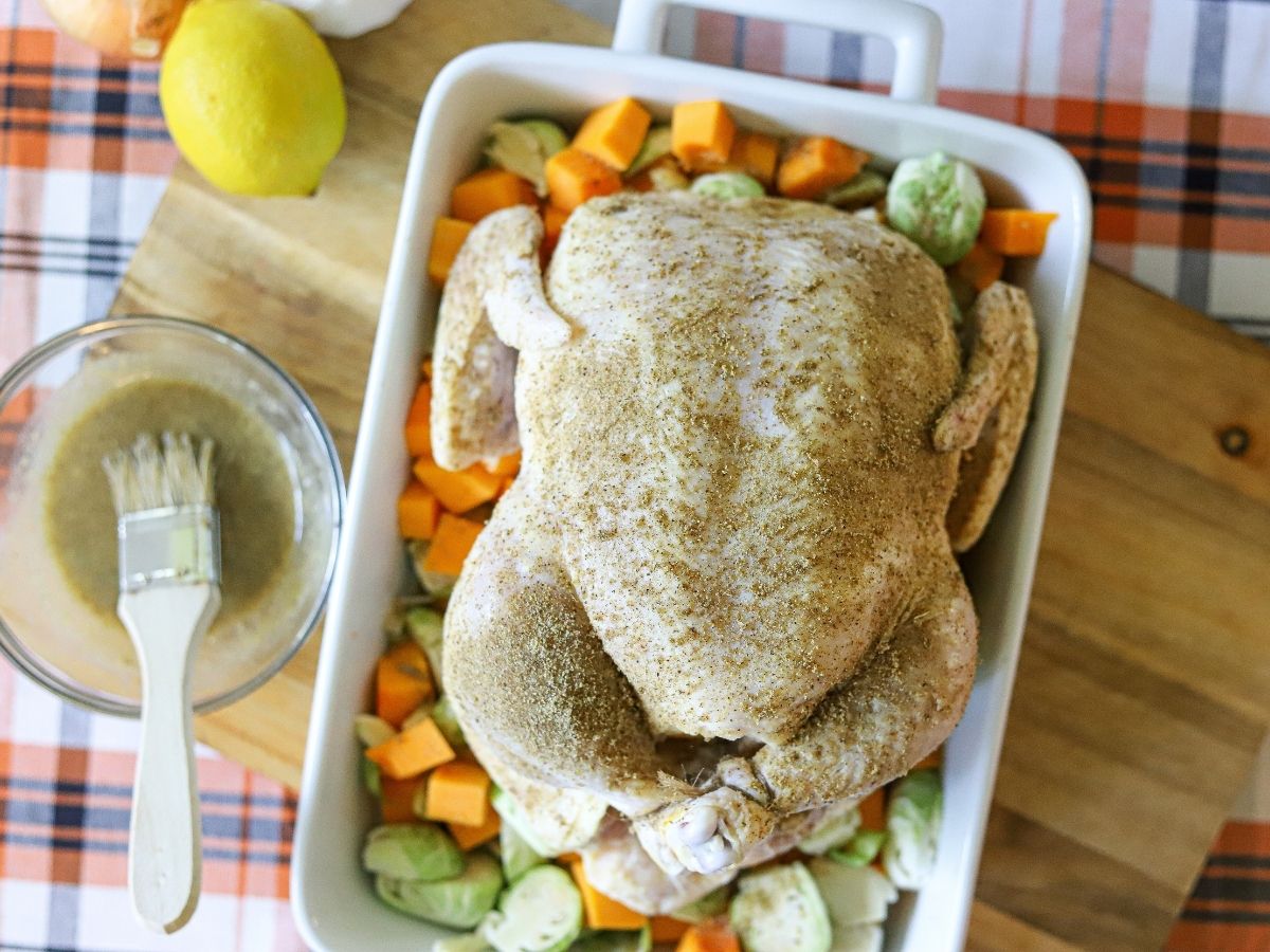 a seasoned whole chicken in a baking dish over a bed of butternut squash and brussels sprouts