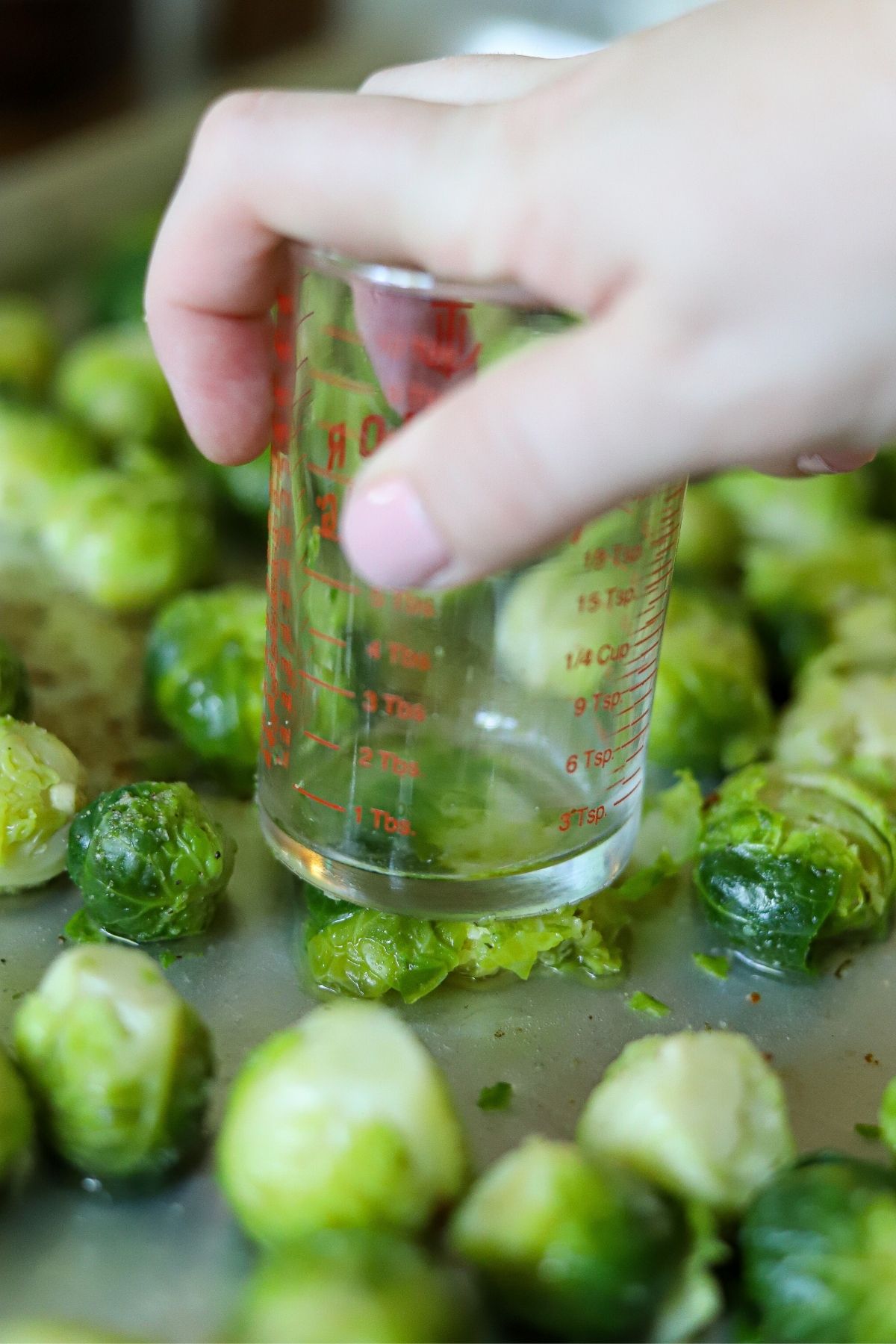 Brussels sprouts on a sheet pan, being smashed with the bottom of a cup.