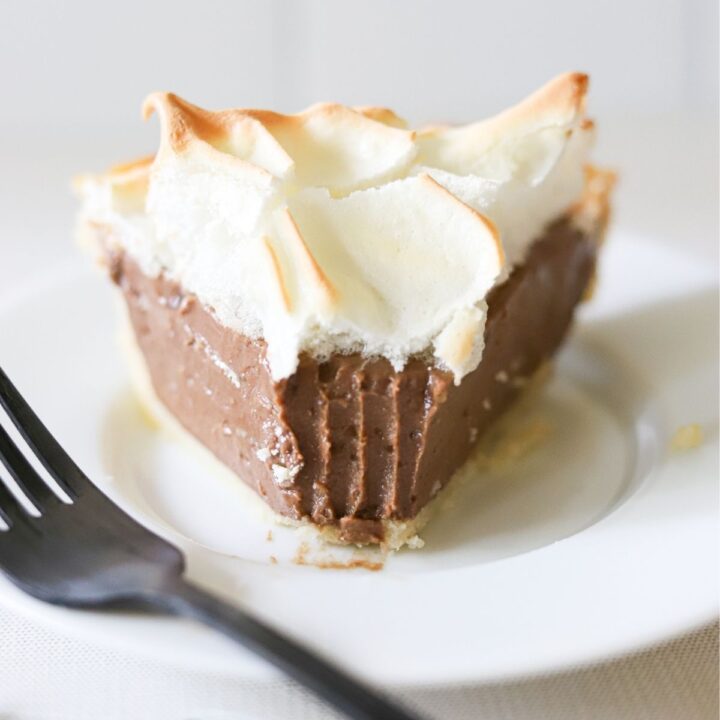 A slice of chocolate cream pie on a white plate, topped with meringue.