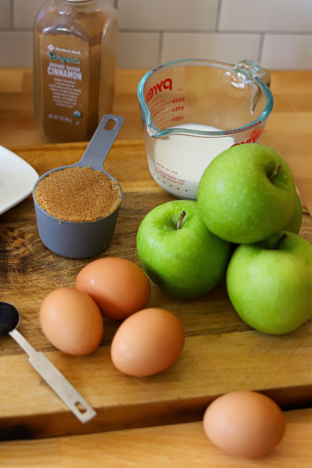 ingredients for gluten free apple cake including granny smith apples, brown sugar, eggs, almond flour, milk, cinnamon, and vanilla.