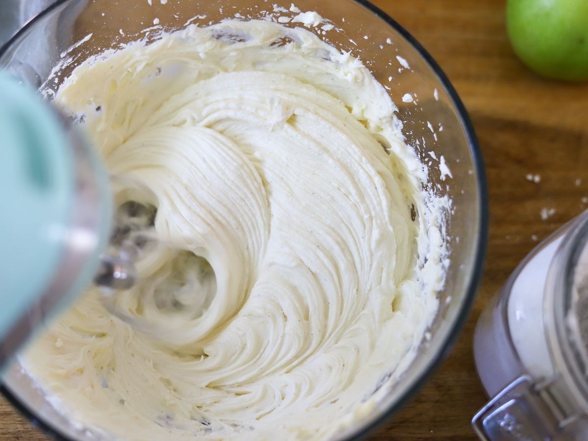 Cream cheese frosting being mixed in a bowl with an electric mixer. 