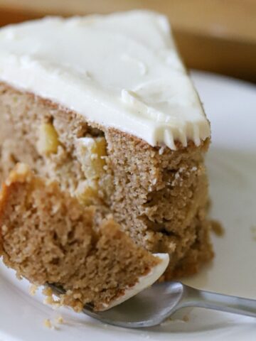 a slice of apple cake with cream cheese frosting on a white plate
