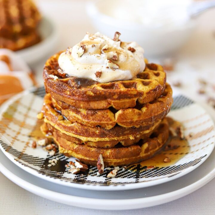 low carb pumpkin waffles stacked and topped with pecans and whipped cream