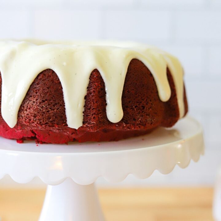 a close up of cream cheese glaze sliding down the side of a red velvet cake.