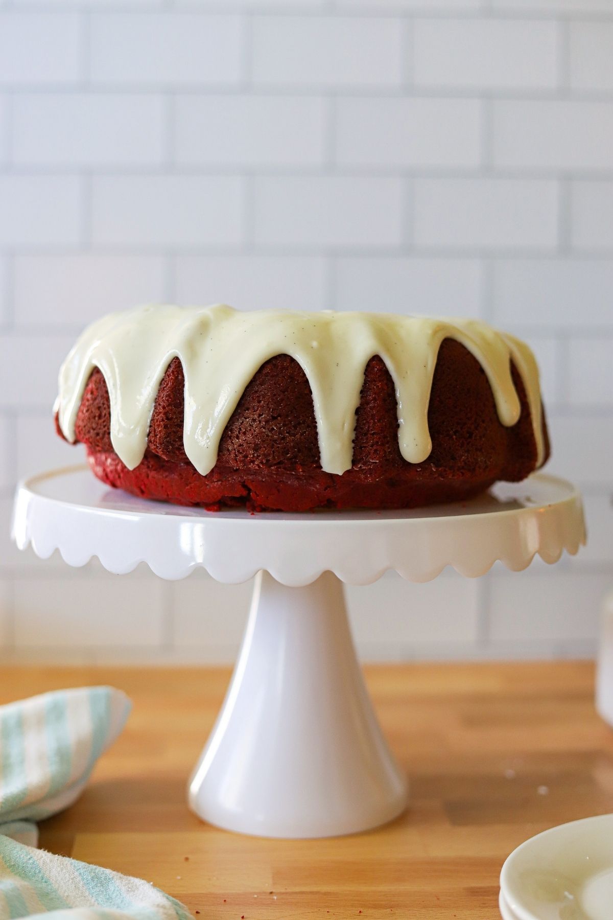 a red velvet cake baked in a bundt pan, topped with cream cheese glaze on a white cake stand