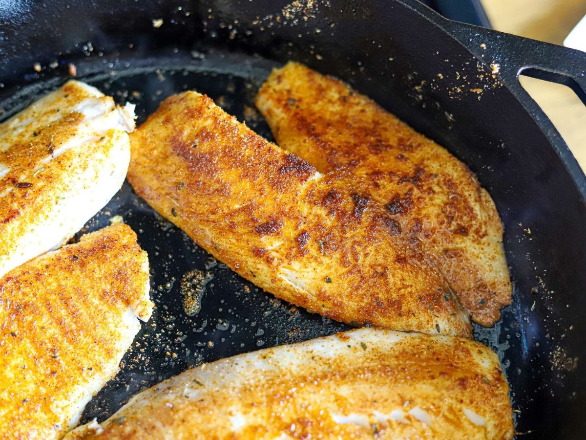 tilapia filets being blackened in a cast iron skillet.