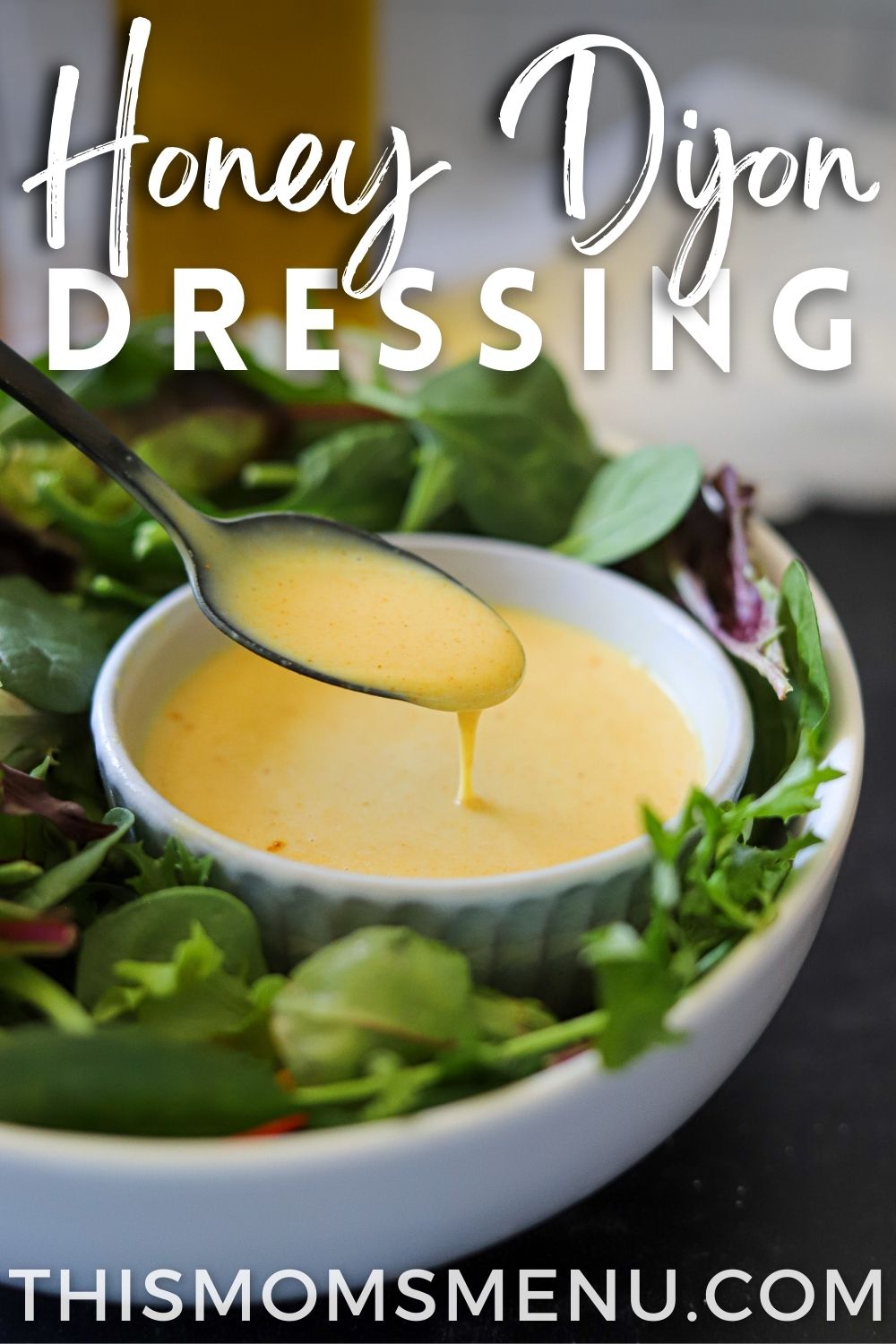 a small bowl full of honey dijon salad dressing in a bowl of salad greens with text overlay