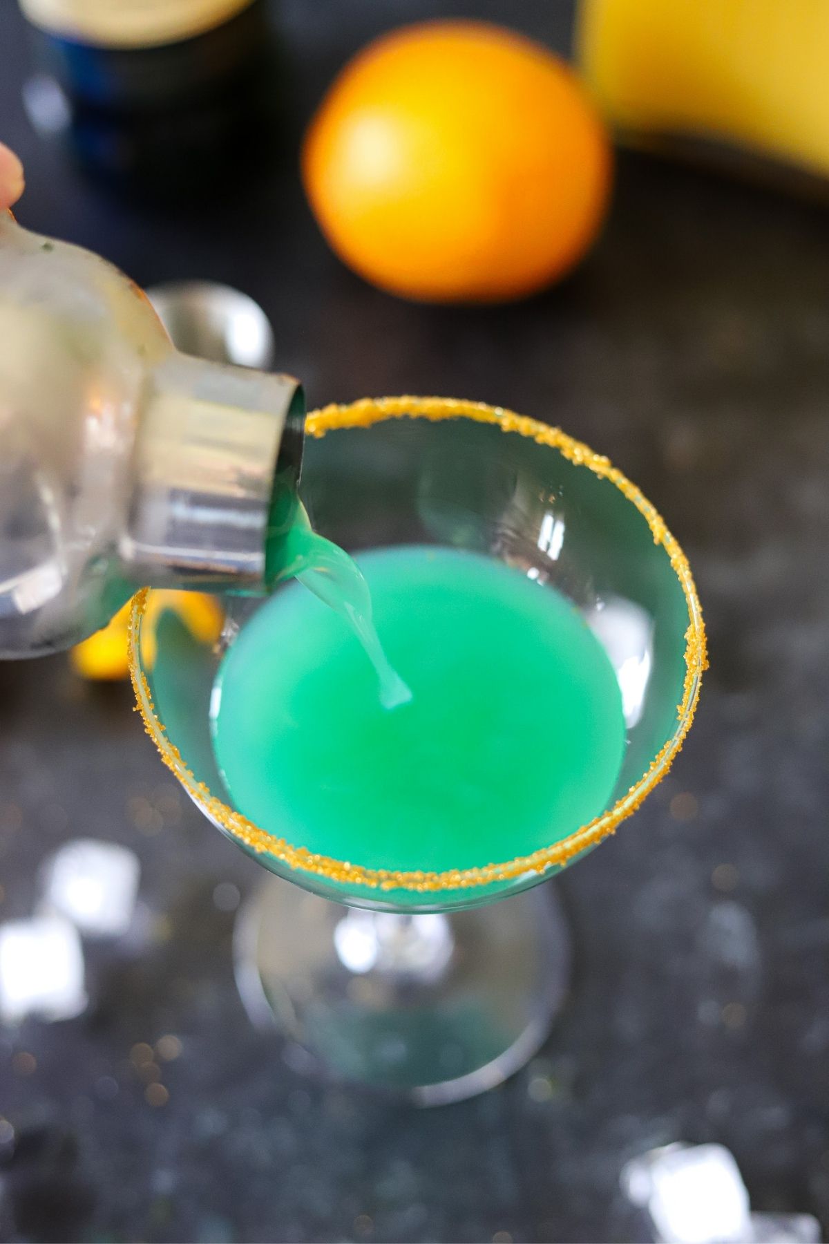 a green cocktail being poured from a cocktail shaker into a coupe glass.