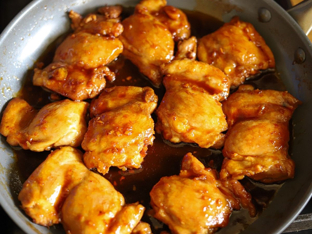 a skillet full of chicken thighs in a sticky Asian glaze