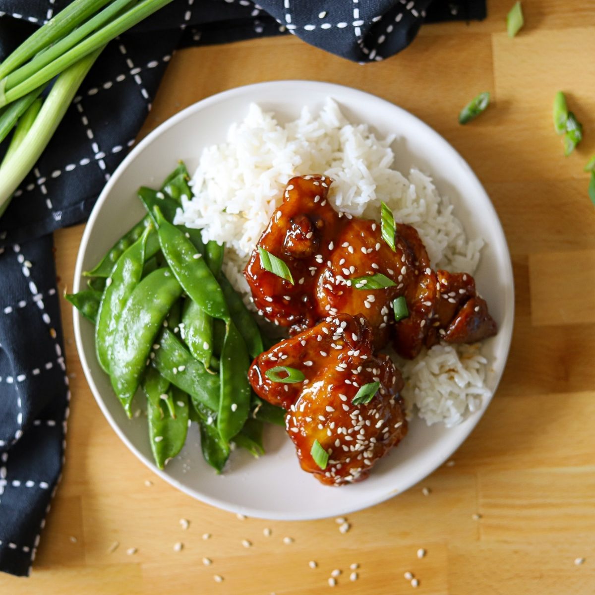 A plate full of white rice, snow peas, and Asian glazed chicken thighs