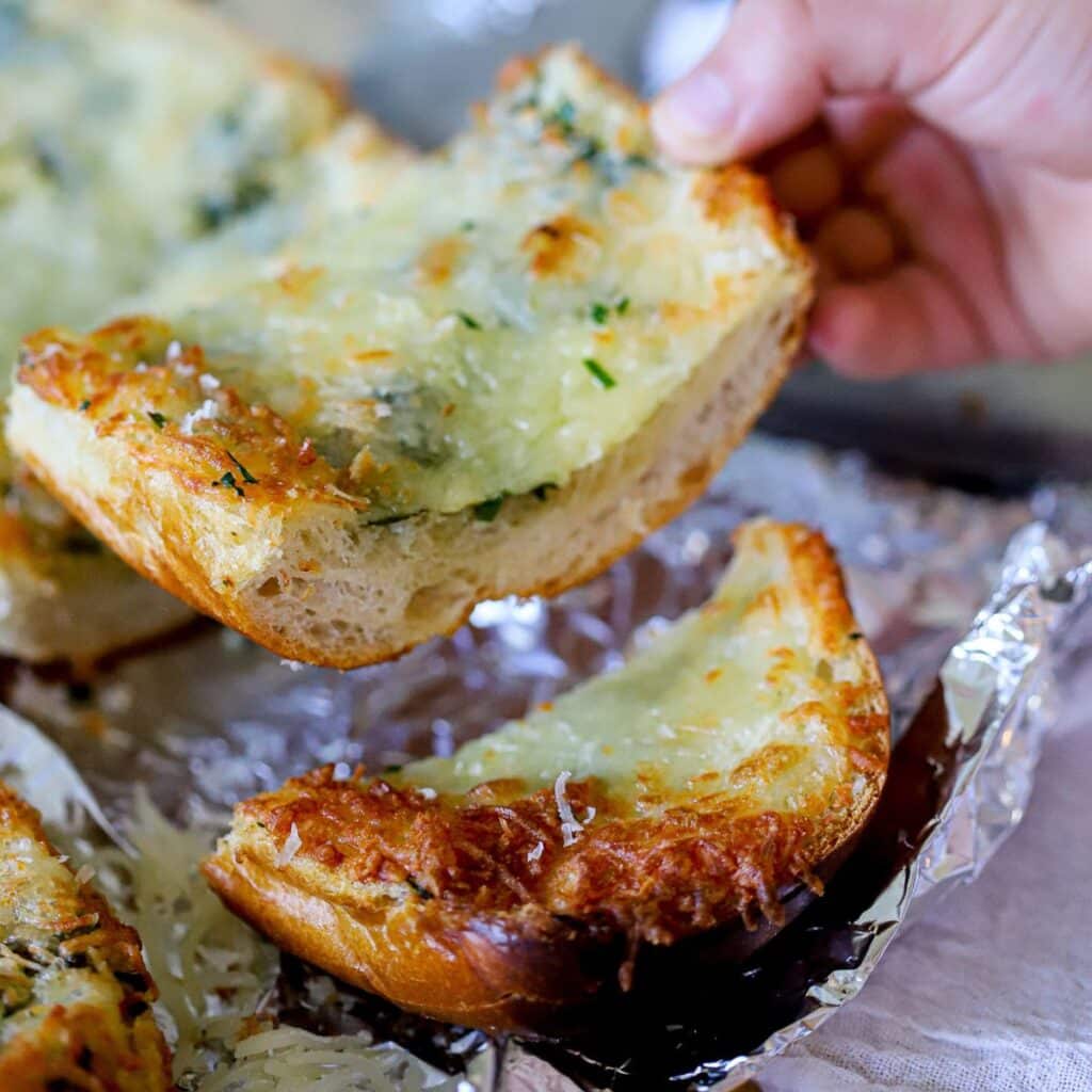 sliced cheesy garlic bread with one being picked up.