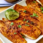 blackened cod fillets on a white plate garnished with fresh parsley and limes