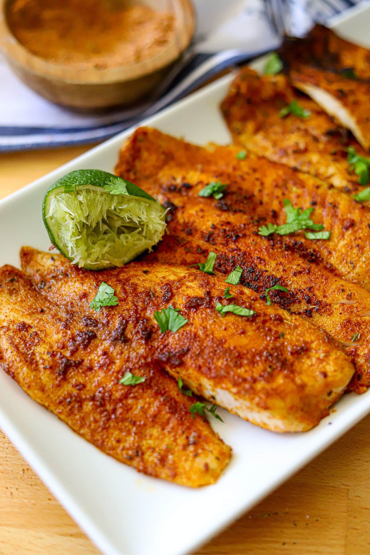 blackened whitefish fillets on a white platter garnished with lime and freshly chopped parsley