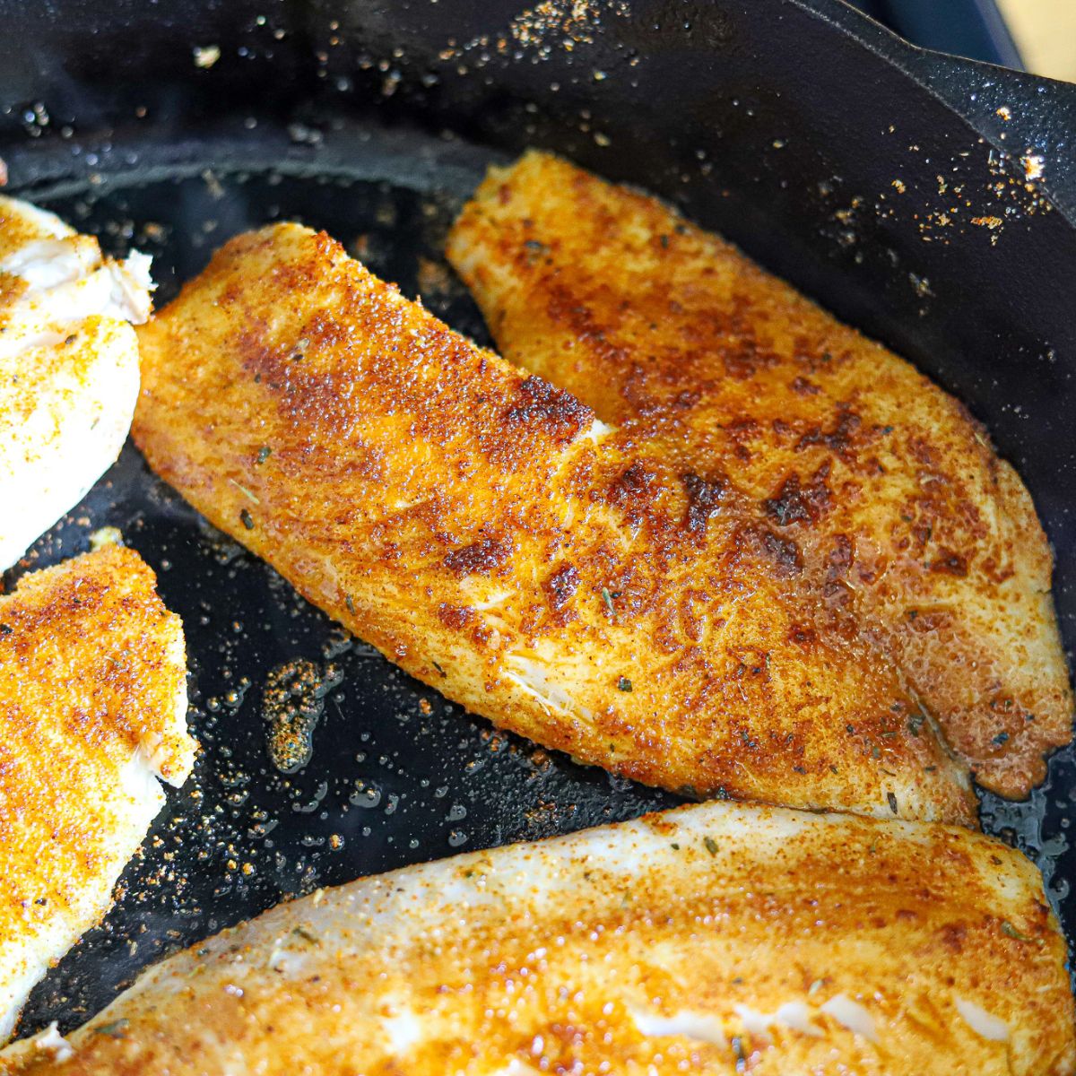 browned tilapia fillets in a cast iron skillet.