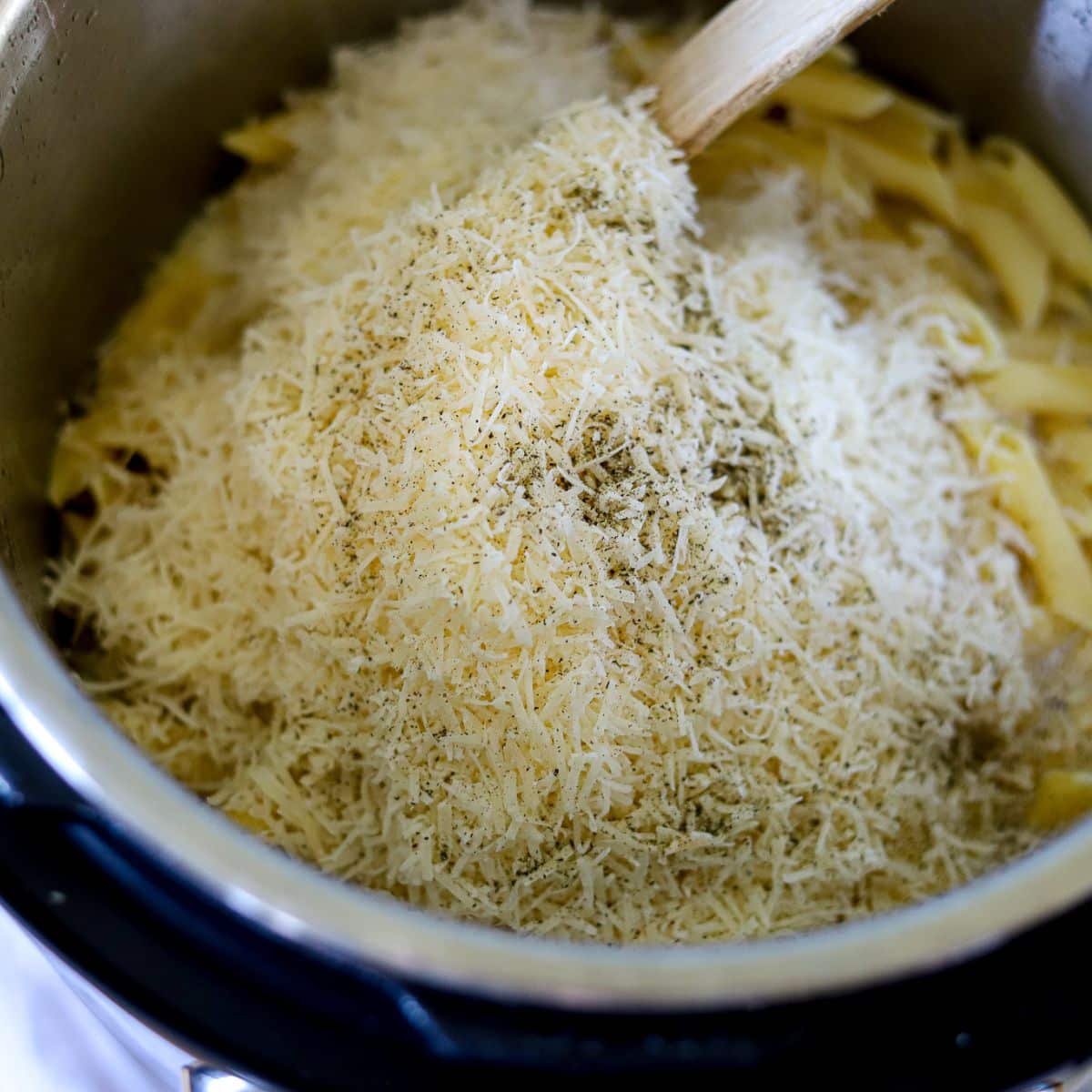 parmesan cheese being stirred into pasta in an instant pot