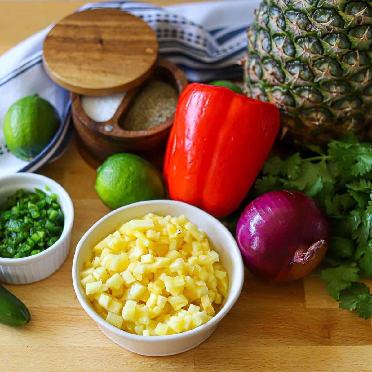 ingredients for homemade pineapple salsa including fresh pineapple, cilantro, red onion, red pepper, limes, salt and pepper.