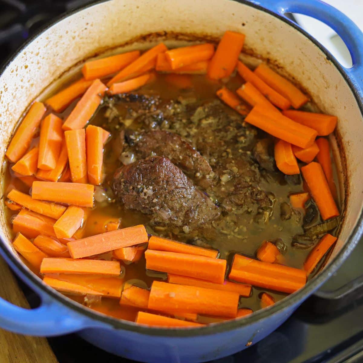 a chuck roast in a dutch oven surrounded by carrots