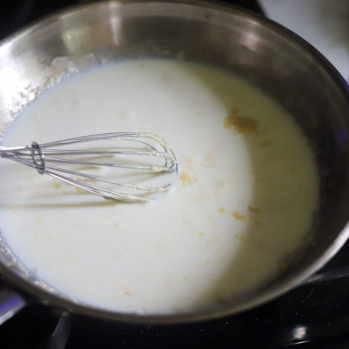milk being whisked into butter and flour for making a sauce.