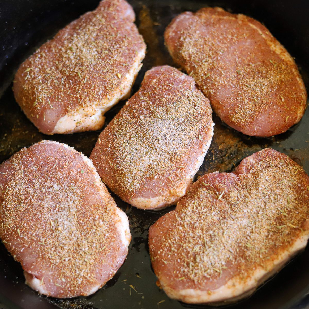 pork chops coated in seasoning cooking in a cast iron skillet.