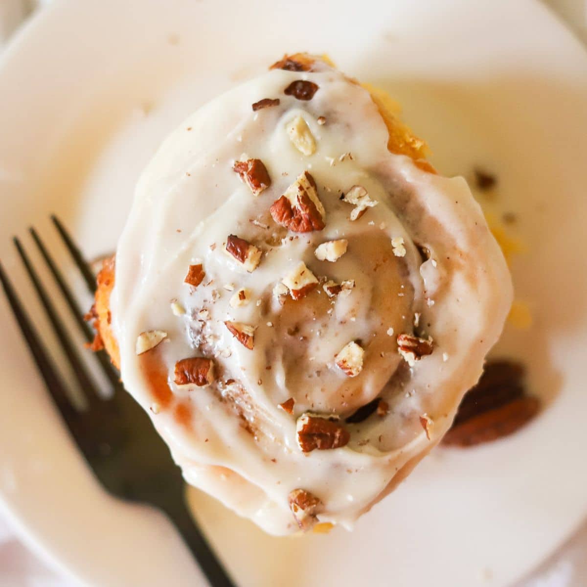 a cinnamon roll from overhead topped with white icing and chopped pecans