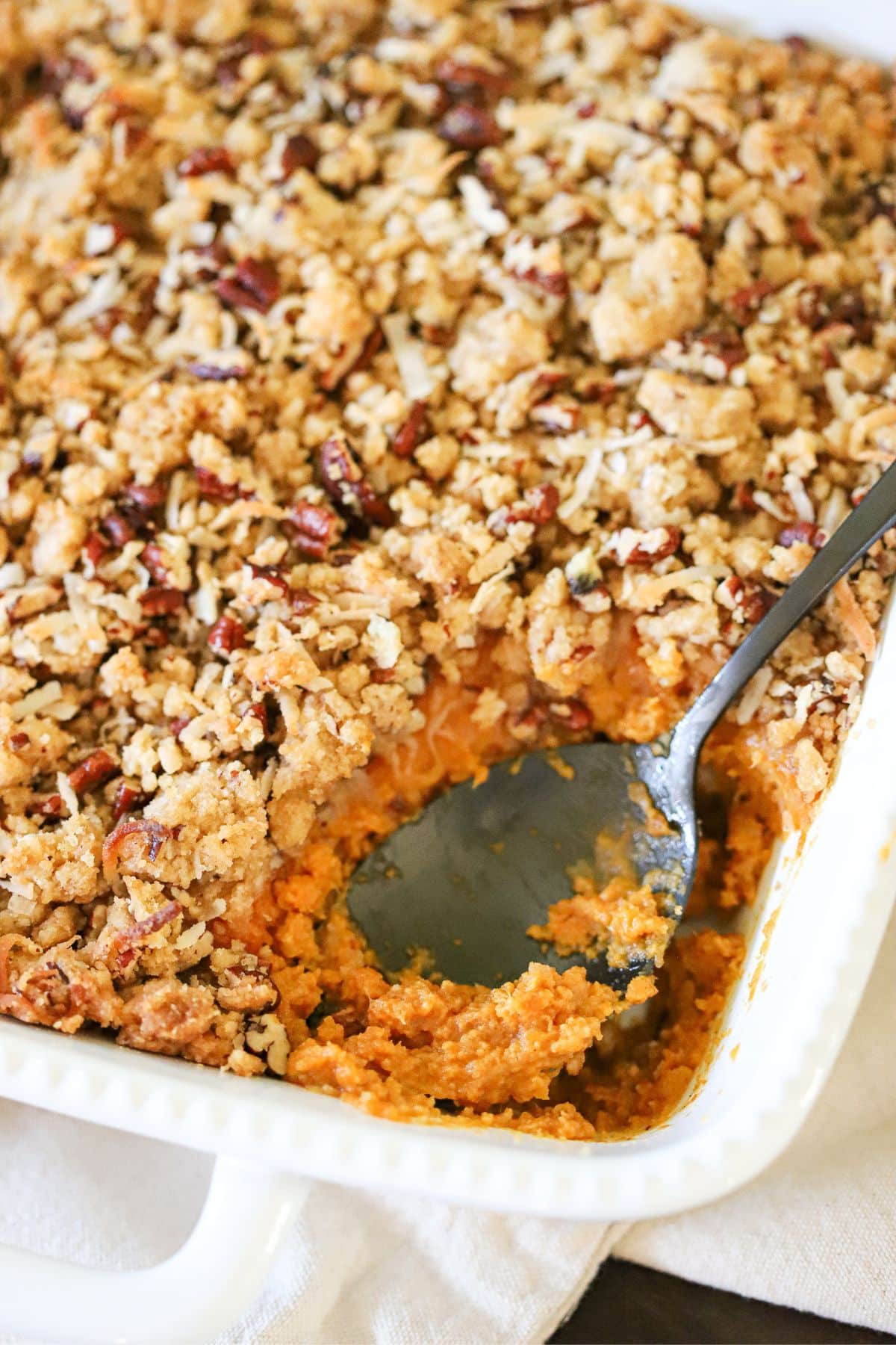 sweet potato crunch casserole in a white dish with a black serving spoon.