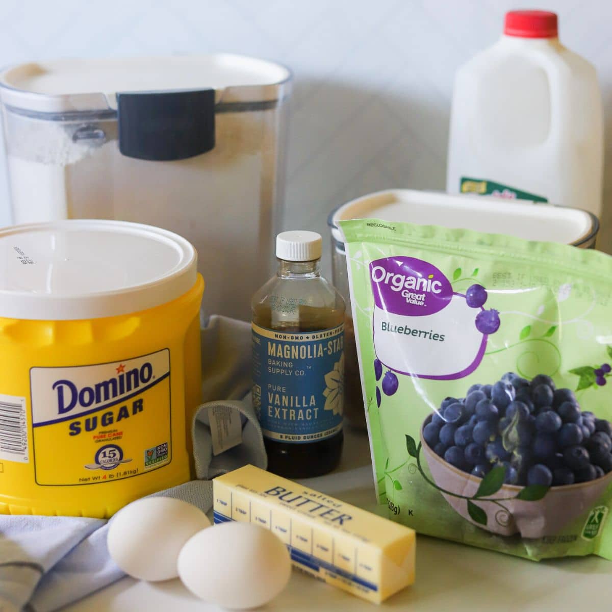 ingredients for homemade blueberry muffins inluding frozen blueberries, sugar, butter, eggs, buttermilk, vanilla, and flour