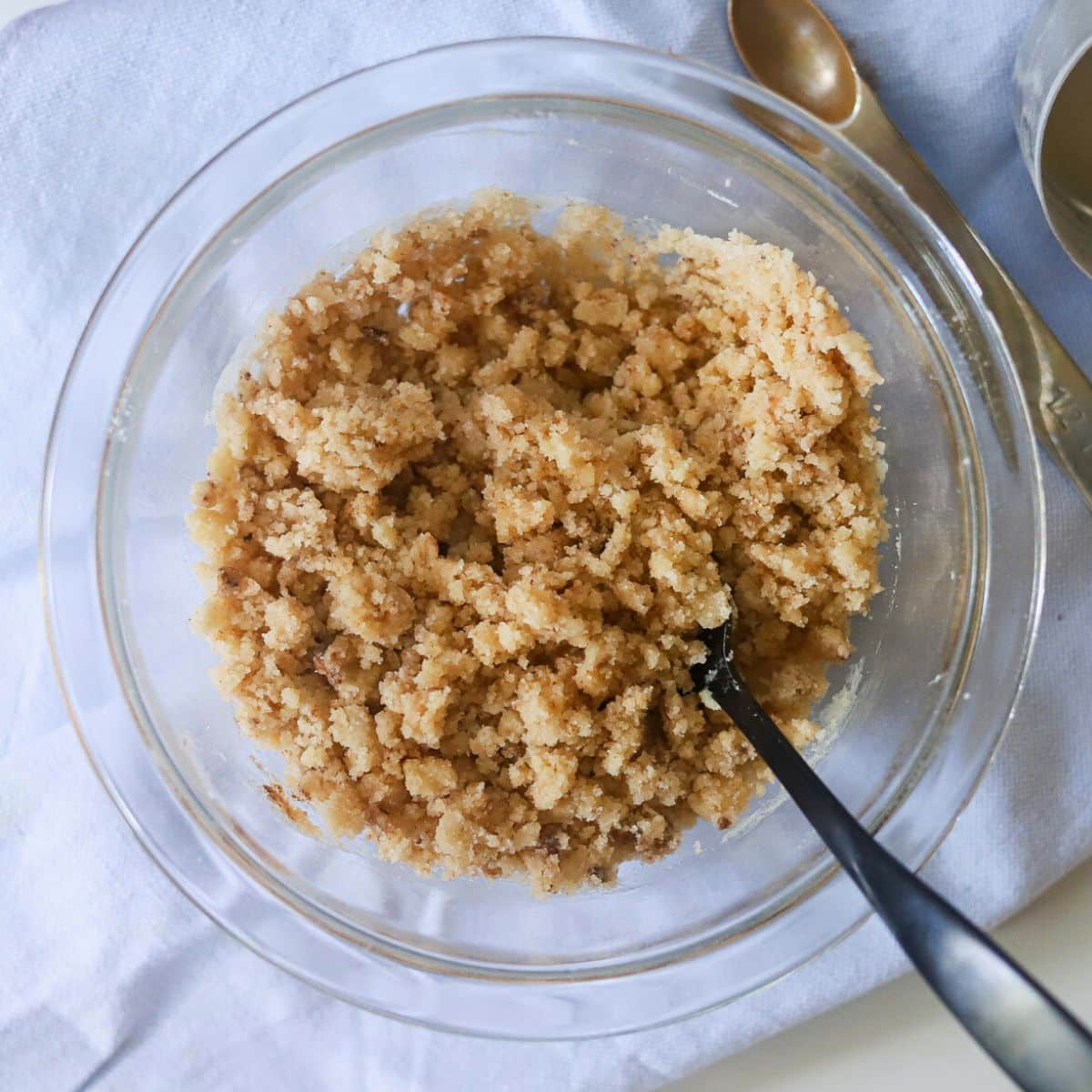 a glass bowl filled with an uncooked crumble topping and a black utensil.