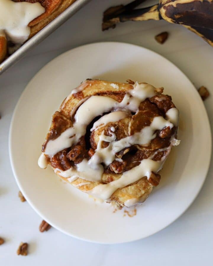 A banana cinnamon roll on a plate topped with vanilla icing