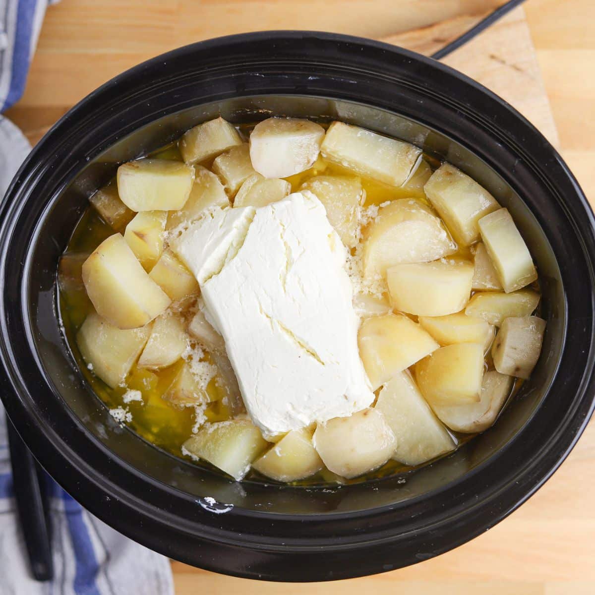 cooked potatoes in a crock pot topped with cream cheese