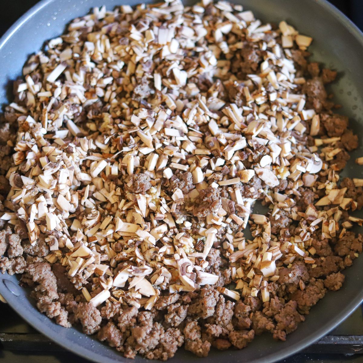 Ground beef in a skillet with mushrooms and garlic.