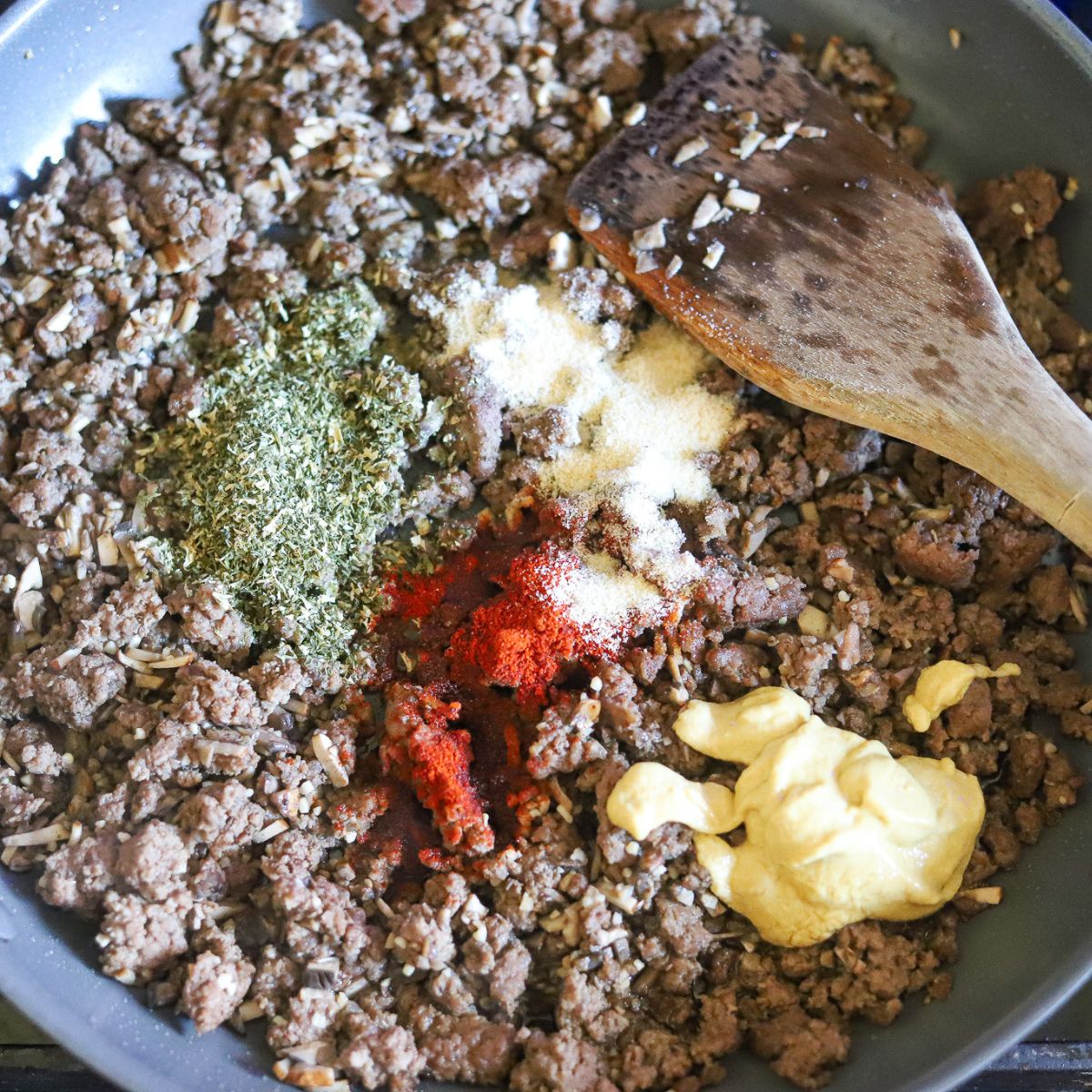 cooked ground beef in a skillet topped with seasonings and mustard.