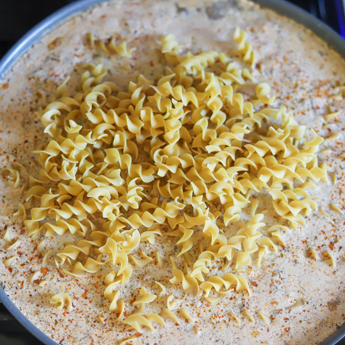 a skillet full of ground beef and cream topped with egg noodles.
