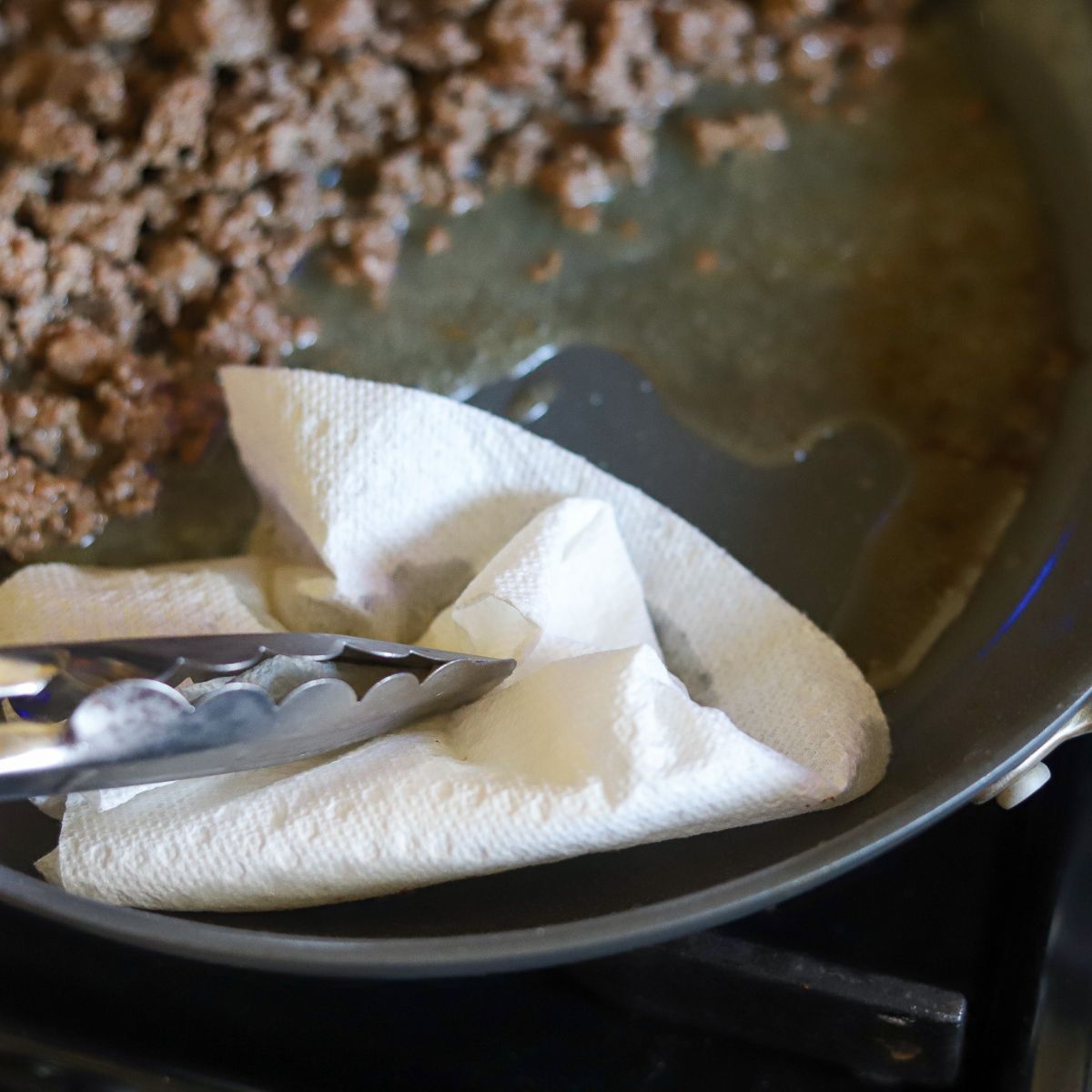 ground beef in a skillet being drained with a paper towel
