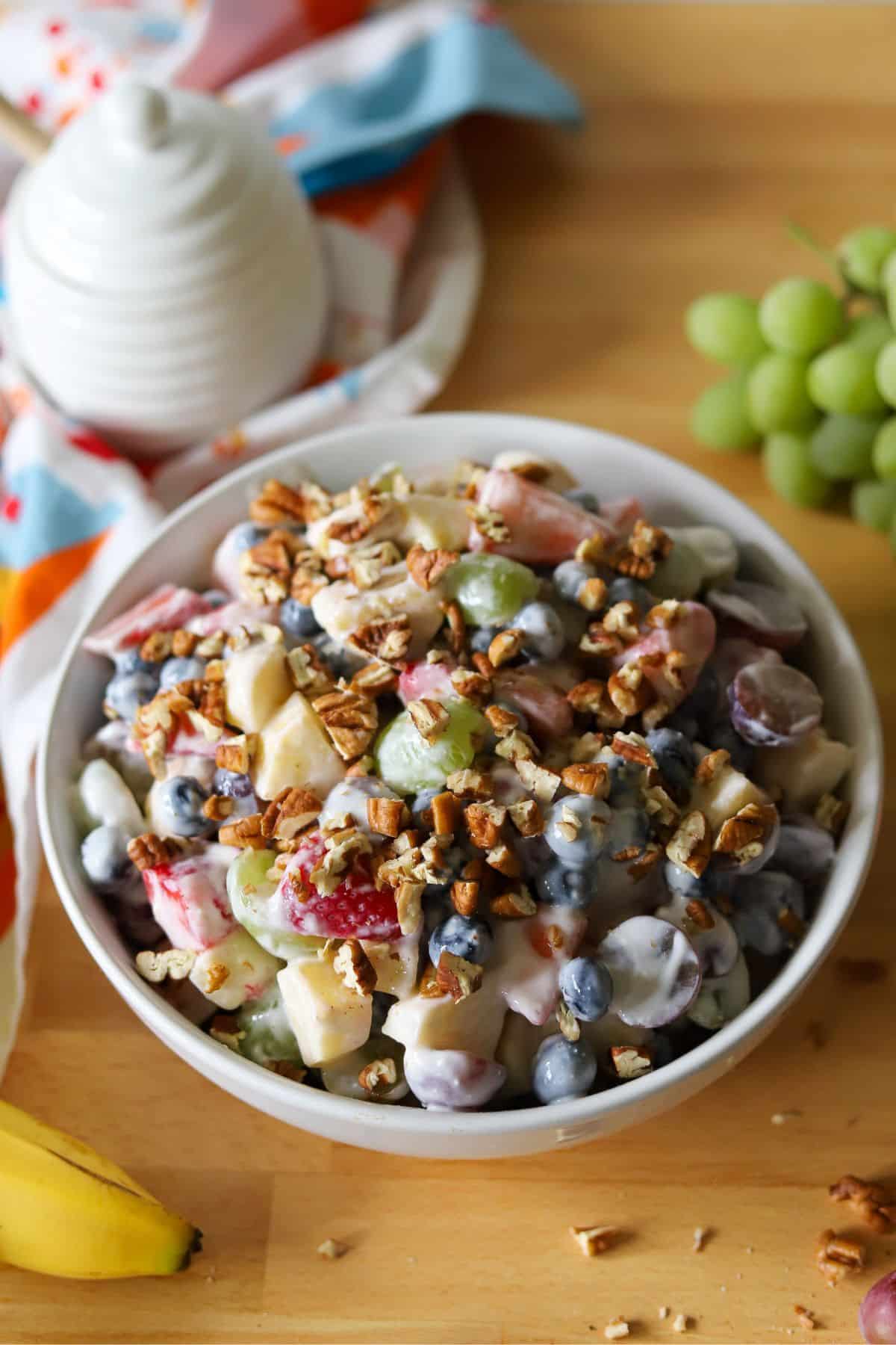 a bowl of fruit salad topped with pecans and coated in a creamy honey yogurt dressing. 