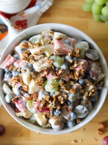 a bowl of fruit salad coasted in. a creamy yogurt sauce and topped with pecans