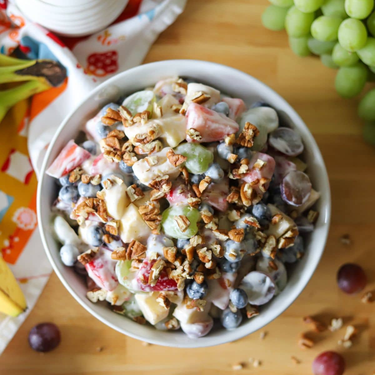a bowl of fruit salad coasted in. a creamy yogurt sauce and topped with pecans