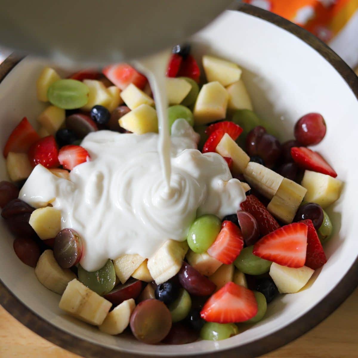 honey yogurt being poured over sliced fruit in a large bowl.
