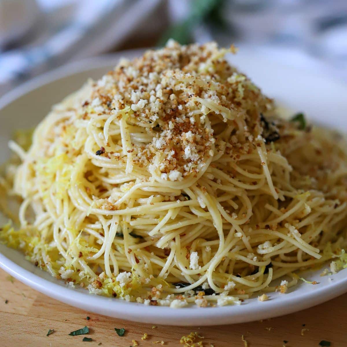 Garlic and lemon pasta topped with toasted breadcrumbs on a while plate.