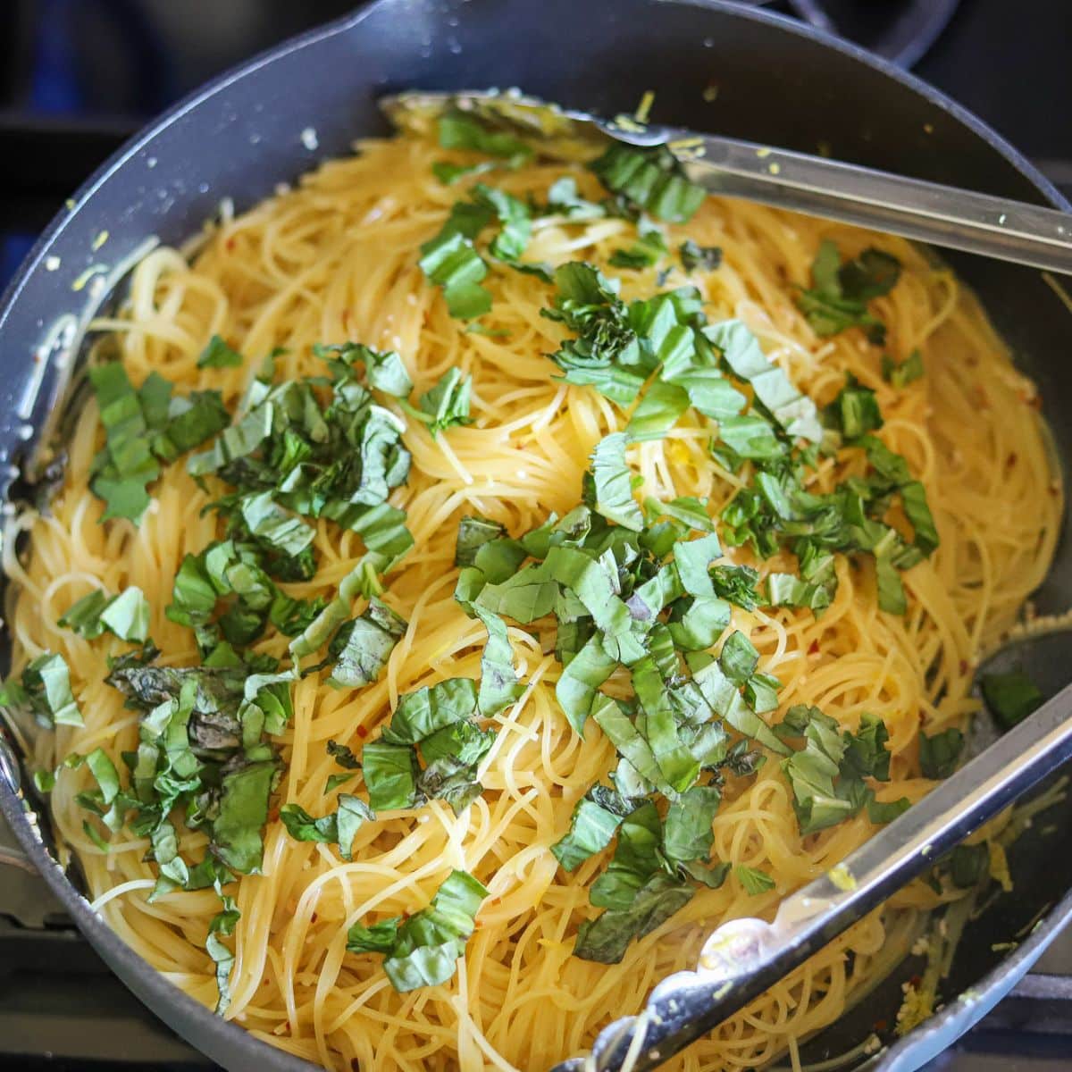 Lemon pasta in a large skillet with fresh basil being stirred in