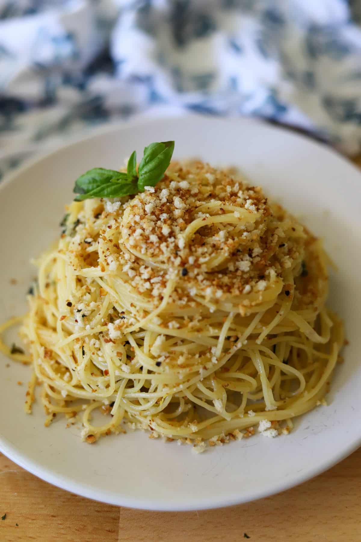 a plate full of garlic lemon pasta topped with toasted breadcrumbs and a sprig of fresh basil.