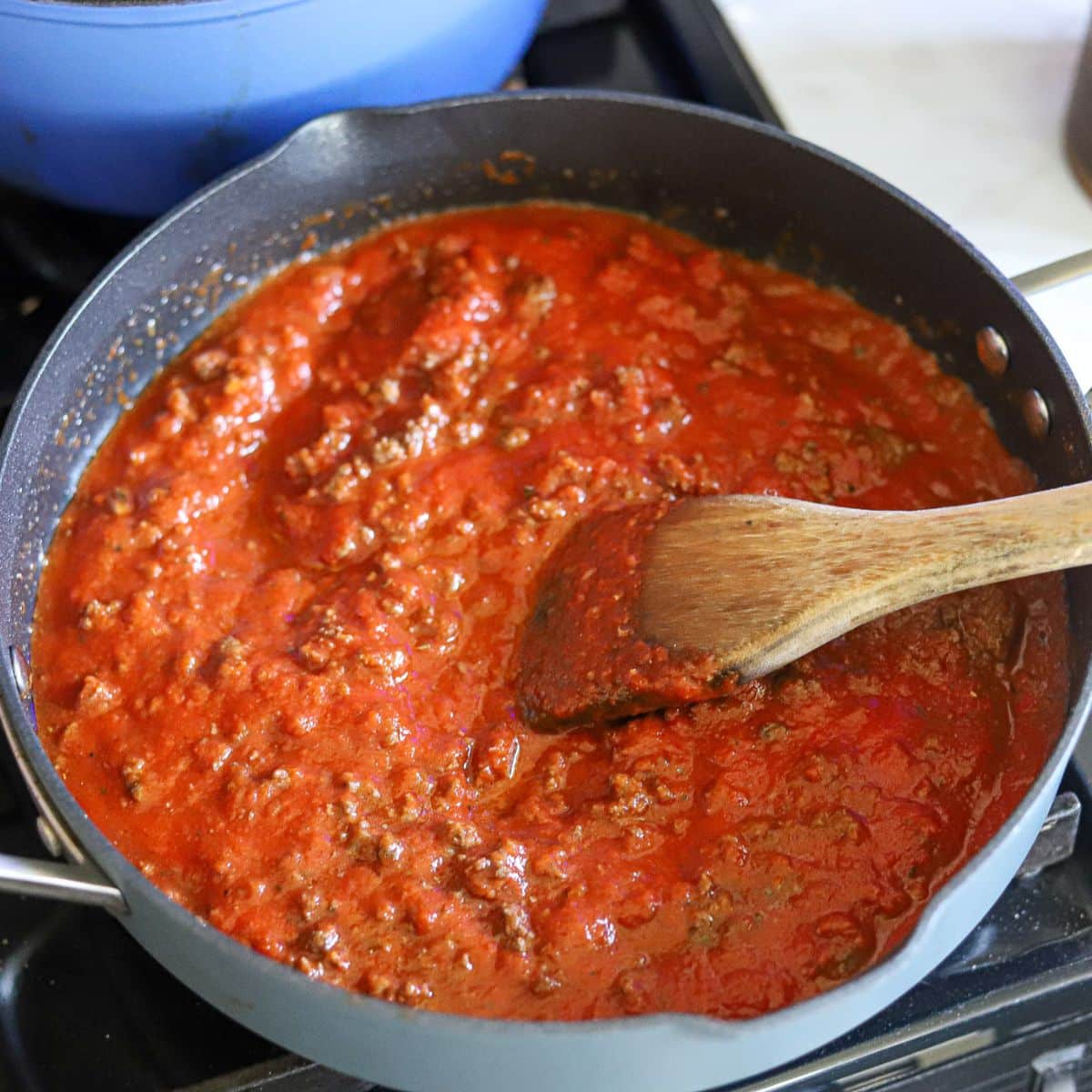 marinara sauce with ground beef in a large skillet with a wooden spoon.