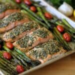 a silver sheet pan filled with asparagus, cherry tomatoes, and salmon filets that are coated in garlic and parsley