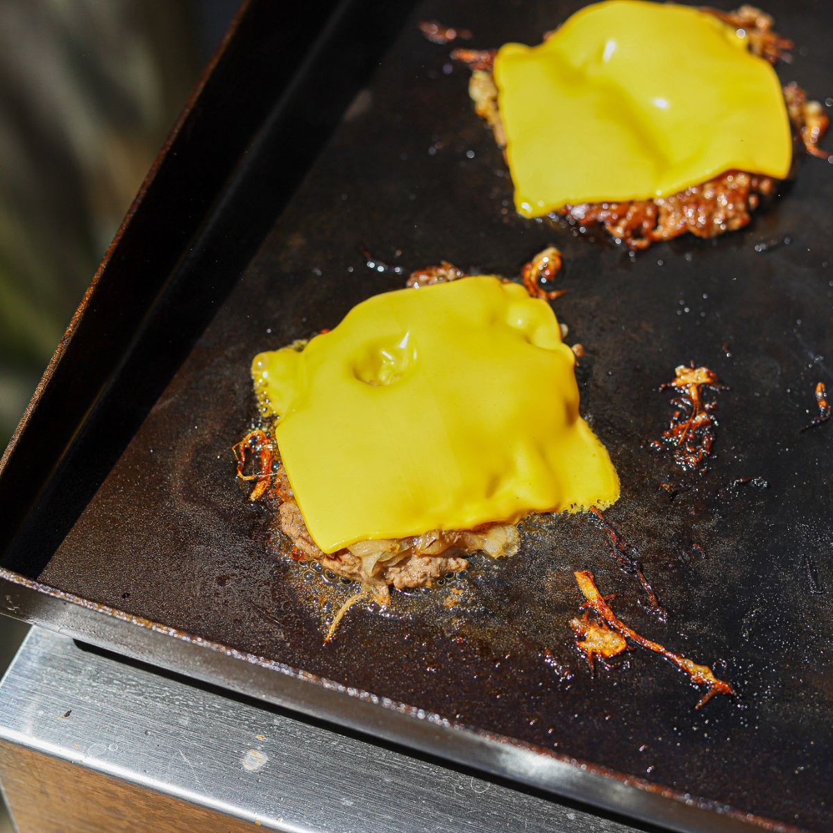 burger patties topped with American cheese on a blackstone griddle 