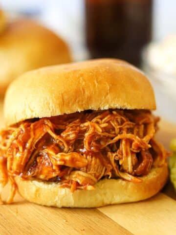 a pulled barbecue chicken sandwich with pickles on the side