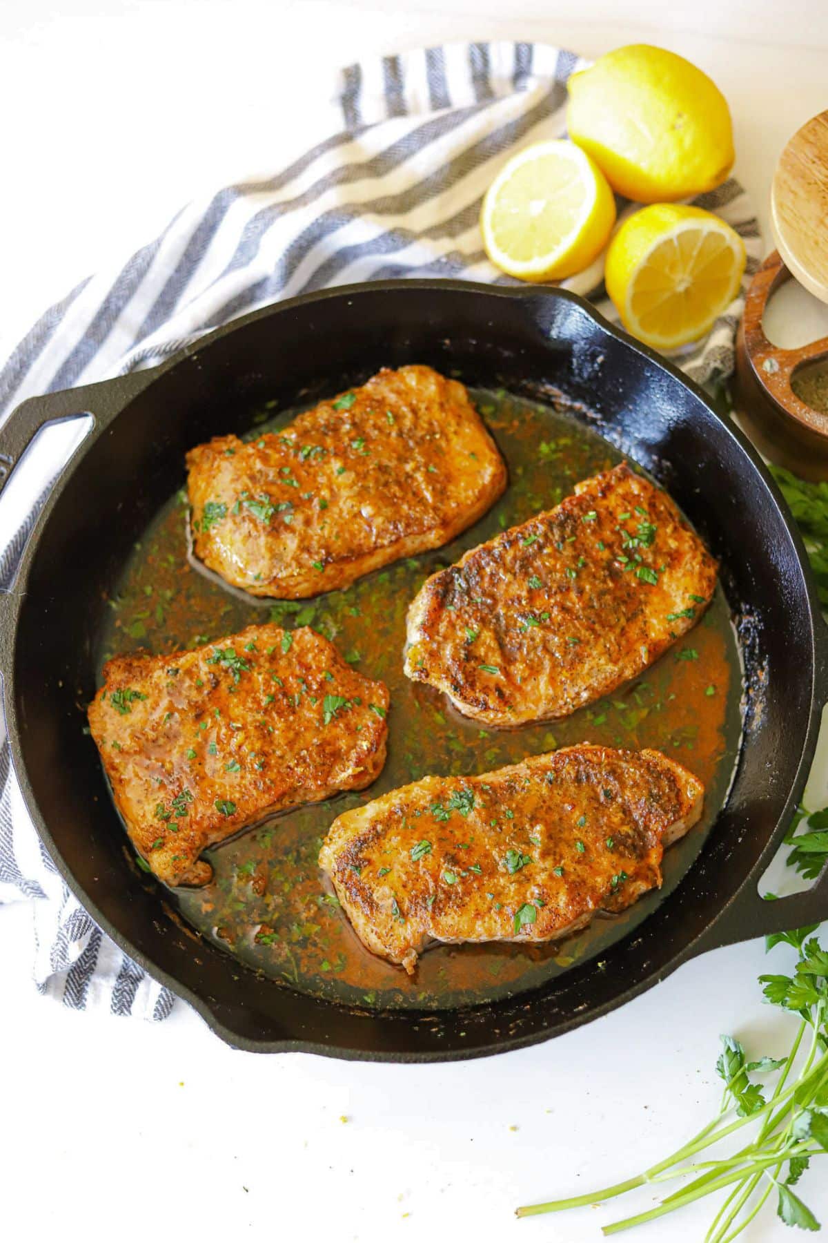 a cast iron skillet with four pork chops in a buttery lemon pepper sauce. 