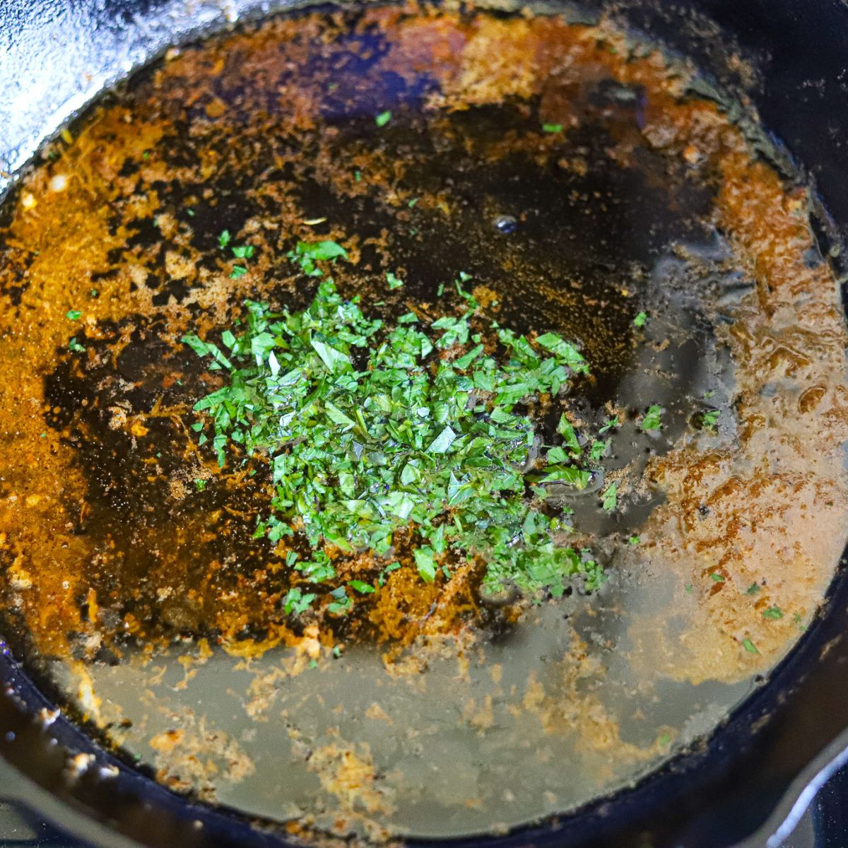 a cast iron skillet filled with melted butter, seasoning, and freshly chopped parsley.