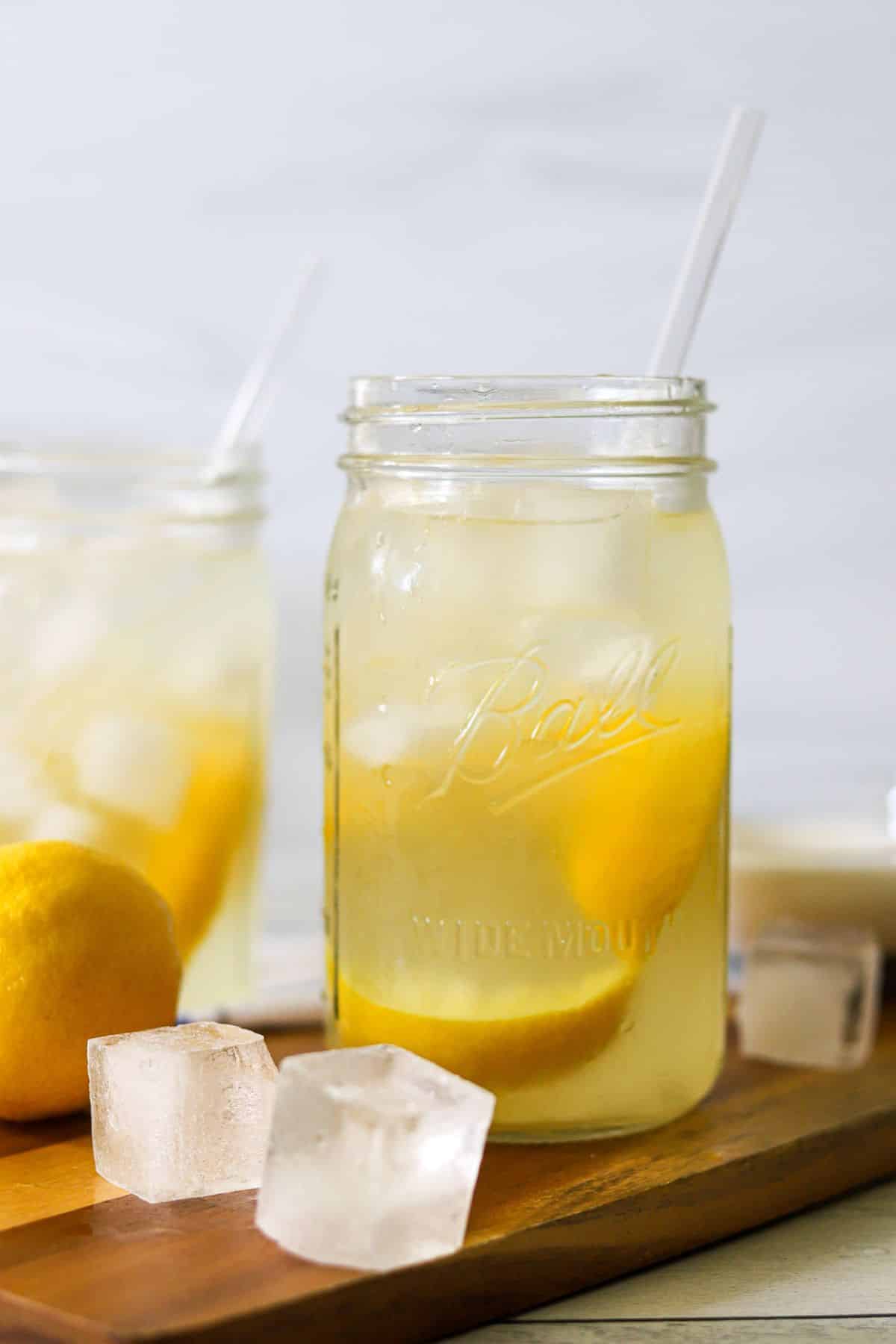 two mason jars filled with ice, lemon wedges, and lemonade for a classic state fair, shaken lemonade
